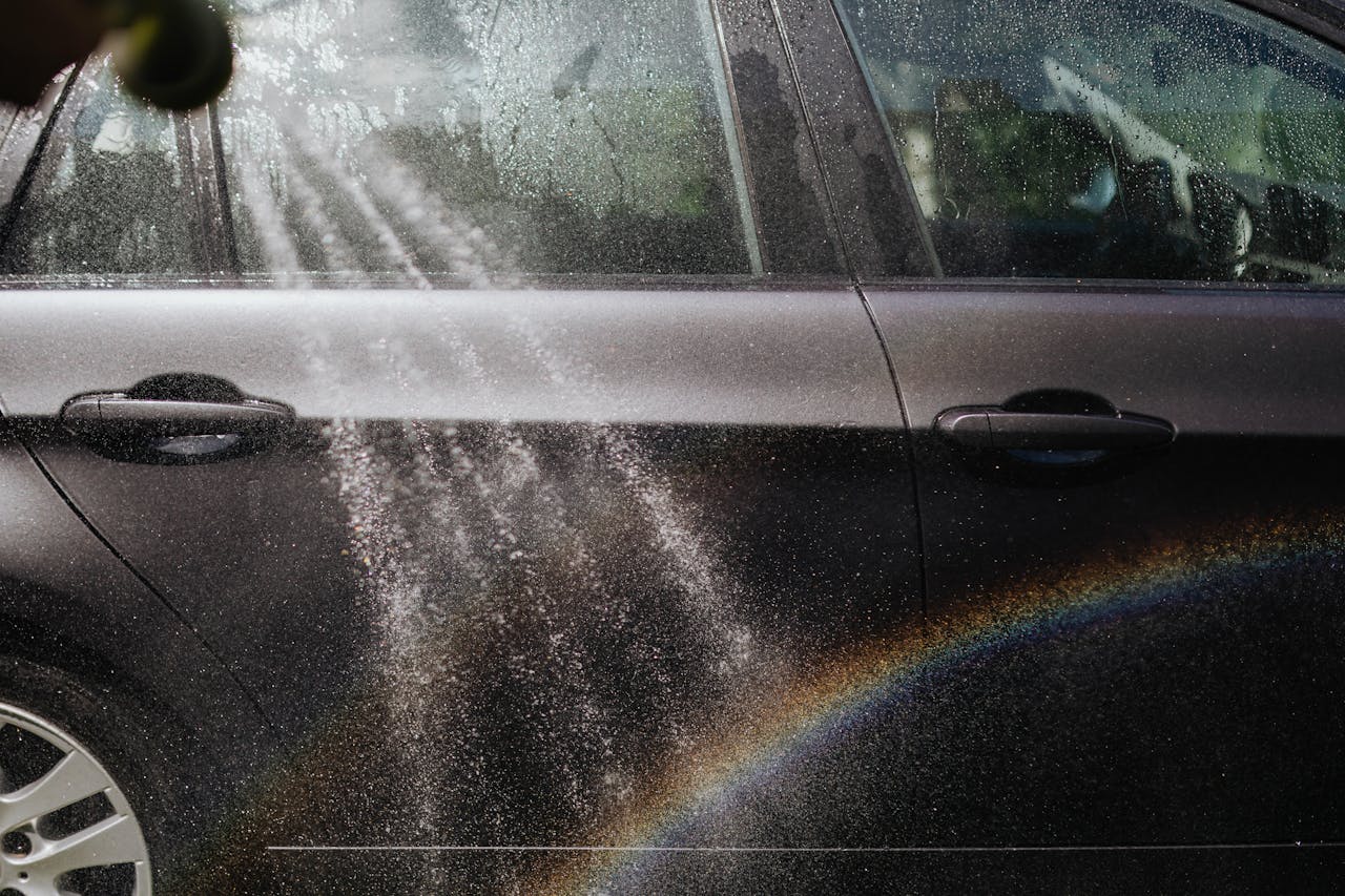 about-us Close-up of a car being washed with a visible rainbow in sunlight.